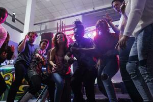 Jeune gens dansant et sauter ensemble sur piste de dance dans boîte de nuit. diverse Hommes et femmes copains faire la fête et aller en boîte à club fête tandis que profiter vie nocturne divertissement photo