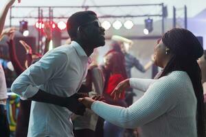 insouciant africain américain couple dansant ensemble et ayant amusement dans boîte de nuit. de bonne humeur Jeune homme et femme clubbers en portant mains et faire la fête sur piste de dance tandis que aller en boîte photo