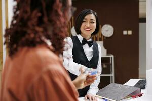 femme payant pour pièce réservation à Hôtel réception, en utilisant carte et pos Terminal pour électronique Paiement à de face bureau comptoir. employé en gardant des dossiers de réservation demandes de renseignements à vérifier dehors. photo