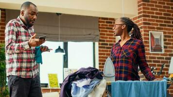 moderne épouse avoir fatigué et en colère à propos Faire corvées seul, repassage vêtements avec vapeur outil dans appartement. Jeune la personne étant malheureux et irrité à propos travaux ménagers. ordinateur de poche tir. photo