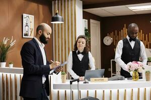 entrepreneur arrivée dans Hôtel réception, signature formes à S'inscrire et vérifier dans. professionnel homme avec vêtements de cérémonie et valise rester à luxe recours à assister important affaires réunions. photo