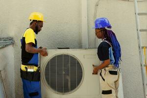 africain américain ingénierie collègues de travail ouverture en haut rouillé en dehors de un service air Conditionneur à remplacer il avec Nouveau performant à l'extérieur condenseur après évacuation réfrigérant et remplacer conduits photo