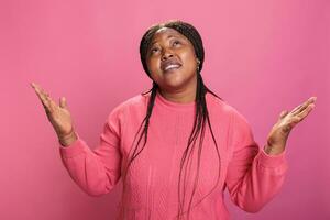 fidèle catholique femme dans rose pull permanent avec paumes face à ciel plaidoirie et mendicité à le pardon. religieux africain américain Jeune adulte prier pour une mieux la vie plus de rose Contexte photo