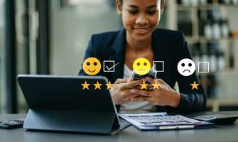 concept d'évaluation du service client. femme d'affaires appuyant sur le visage sourire émoticône spectacle sur écran virtuel sur tablette et smartphone au bureau photo
