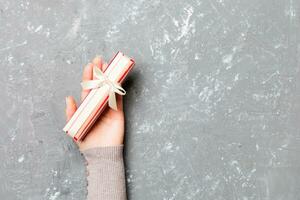 plat allonger de femme mains en portant cadeau enveloppé et décoré avec arc sur gris ciment Contexte avec copie espace. Noël et vacances concept photo