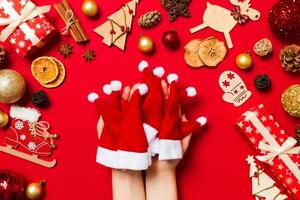 vue de dessus des mains féminines tenant une pile de chapeaux de père noël sur fond rouge. décorations du nouvel an. concept de vacances de noël photo