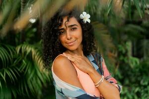 proche en haut portrait de bienheureux femme avec plumeria fleur dans Cheveux après spa dans luxe station balnéaire. portant boho tropical tenue. photo