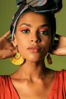 beauté portrait de noir africain américain femme dans Orange Vêtements et ethnique tête emballage je poing dans studio. brillant faire en haut. photo
