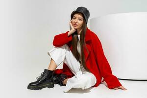 à la mode modèle dans élégant chapeau, rouge manteau et bottes posant sur blanc Contexte dans studio. photo