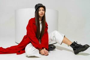 à la mode modèle dans élégant chapeau, rouge manteau et bottes posant sur blanc Contexte dans studio. photo