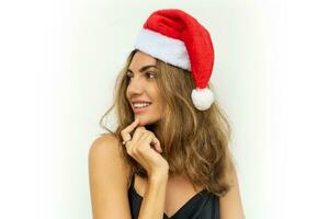proche en haut portrait de magnifique brunette souriant femme dans rouge Père Noël chapeau posant sur blanc Contexte. portant élégant noir robe. photo