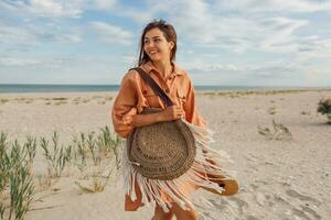 une femme dans un Orange robe et chapeau sur le plage photo