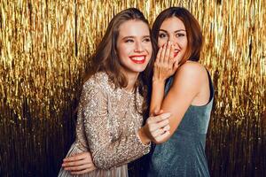 proche en haut studio image de deux incroyable sexy célébrer les filles avec rouge lèvres, surprise affronter, en riant , posant sur d'or scintillant Contexte. Nouveau année fête ambiance. photo