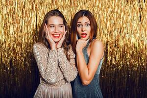 proche en haut studio image de deux incroyable sexy célébrer les filles avec rouge lèvres, surprise affronter, en riant , posant sur d'or scintillant Contexte. Nouveau année fête ambiance. photo