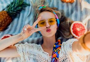 excité fille fabrication selfie sur plage serviette. boho accessoires. Jaune lunettes de soleil.top voir. photo