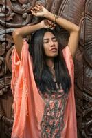 étourdissant asiatique femme dans boho ethnique robe posant plus de bois ornemental Contexte. photo