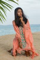 romantique asiatique femme posant sur tropical plage. parfait peau. robe avec broderie. photo