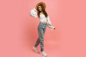 plein longueur image de payant femme dans élégant lin Haut avec ballon manches et bleu jeans posant sur rose Contexte. été mode les tendances. photo