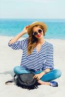 proche en haut mode de vie été portrait de Frais Jeune femme dans cool des lunettes de soleil et paille chapeau séance sur le ensoleillé tropical plage. profiter sa vacances . photo