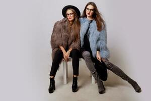 studio mode portrait de deux élégant femmes dans élégant hiver rose fourrure manteau et branché lunettes. photo