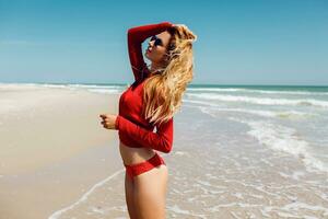 content blond femme dans l'eau souriant content en marchant vers caméra. liberté et vacances concept. incroyable tropical plage. portant rouge bikini. parfait bronzer corps et svelte chiffre. photo