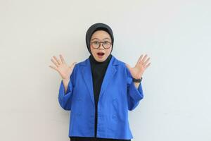 magnifique Jeune asiatique femme portant lunettes, hijab et portant bleu blazer avec surpris visage geste photo