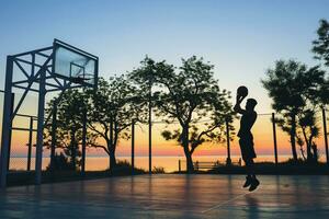 noir homme Faire des sports, en jouant basketball sur lever du soleil, sauter silhouette photo