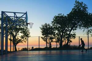 noir homme Faire des sports, en jouant basketball sur lever du soleil, silhouette photo