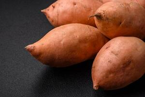 Frais grand rose sucré Patate tubercules avec tomates et épices sur une foncé Contexte photo