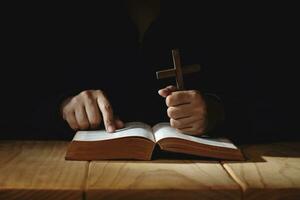 spiritualité, religion et espérer concept. la personne prier par saint Bible et en bois traverser sur bureau. symbole de humilité, supplication, croyez et Foi pour Christian personnes. foncé Ton. photo