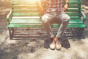 gars hipster assis sur un banc avec un jean et des chaussures de chamois marron. photo