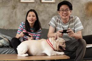 un couple asiatique joue à des jeux vidéo et à un chien de compagnie à proximité. photo