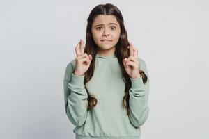 Une adolescente brune a croisé les doigts sur un fond de mur blanc photo