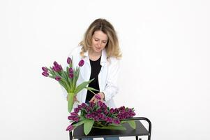 mignonne fille fleuriste dans une chemise recueille une bouquet de violet tulipes pour une cadeau pour de la mère journée photo