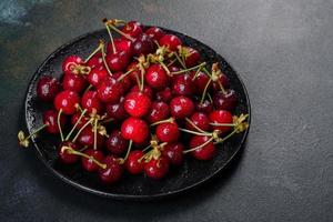 De délicieuses baies de cerises rouges lumineuses fraîches déchirées dans le jardin d'été photo