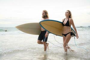 Jeune homme et femme en portant planches de surf prêt à marcher dans le mer à le surf. photo