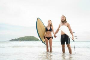 couple de surfeurs en portant mains et à la recherche à chaque autre sur plage photo