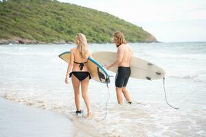 Jeune homme et femme en portant planches de surf prêt à marcher dans le mer à le surf. photo