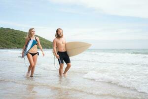 Jeune homme et femme en portant planches de surf prêt à marcher dans le mer à le surf. photo