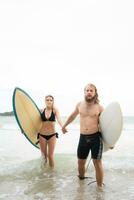 couple de surfeurs en portant mains et à la recherche à chaque autre sur plage photo