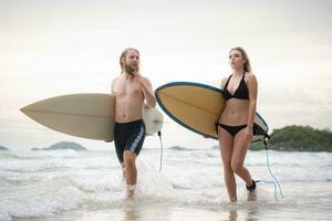 Jeune homme et femme en portant planches de surf prêt à marcher dans le mer à le surf. photo