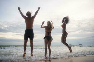 groupe de copains ayant amusement sur le plage à le le coucher du soleil temps. photo