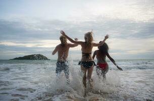 groupe de copains ayant amusement sur le plage à le le coucher du soleil temps. photo