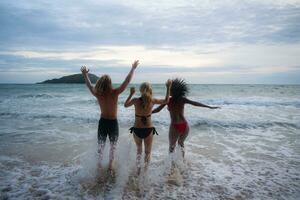 groupe de copains ayant amusement sur le plage à le le coucher du soleil temps. photo