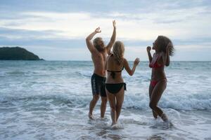 groupe de copains ayant amusement sur le plage à le le coucher du soleil temps. photo