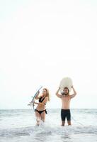 Jeune homme et femme en portant planches de surf sur leur têtes et marcher dans le mer à le surf photo