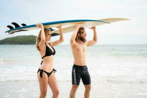 Jeune homme et femme en portant planches de surf sur leur têtes et marcher dans le mer à le surf photo