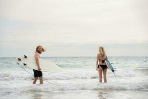 Jeune homme et femme en portant planches de surf prêt à marcher dans le mer à le surf. photo