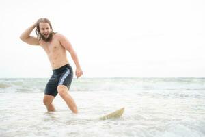 Jeune homme surfant sur le plage ayant amusement et équilibrage sur le planche de surf photo
