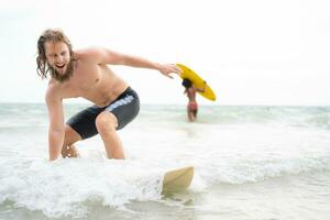 Jeune homme surfant sur le plage ayant amusement et équilibrage sur le planche de surf photo